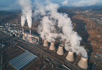 Aerial view of tall chimney pipes with grey smoke from coal power plant. Production of electricity with fossil fuel. Ecology and pollution of nature.