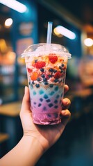 A hand holding a vibrant cup of bubble tea filled with fresh fruit and berries, creating a...