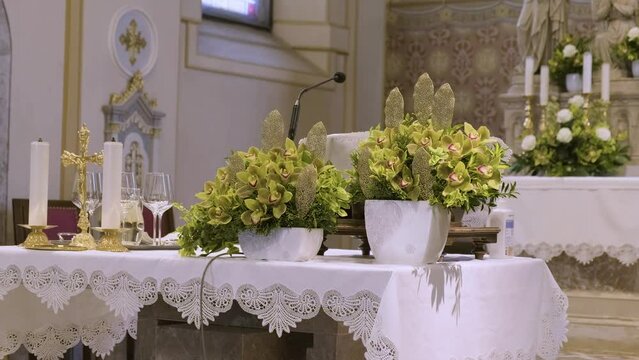 Orbit Around Credence Table With Flowers, Candles, Chalice, Cross Symbols and Microphone on It for Wedding Ceremony, Revealing The Altar With Decorative Flowers, Candles And Statues in The Background.