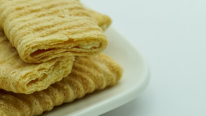 Close-up of stacked crispy, light brown wafer biscuits with visible layers, presented on a white surface. Sweet snack detail.