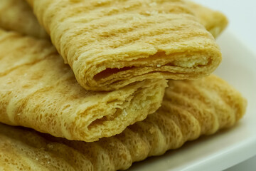 Close-up of stacked crispy, light brown wafer biscuits with visible layers, presented on a white surface. Sweet snack detail.