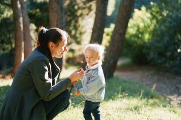 Little girl looks at a flower in her mom hand, crouching next to her in the forest