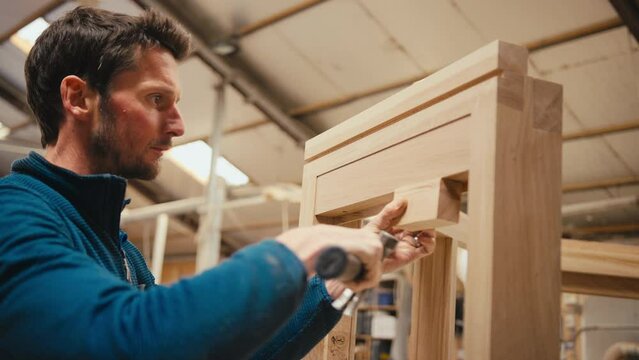 Close up of carpenter hammering piece of wood against window frame in workshop - shot in slow motion
