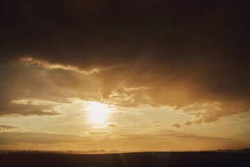 Obraz premium Dark storm clouds and sun over the houses of the evening city