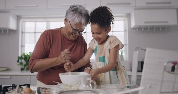 Baking and cooking with a grandmother and her granddaughter during a visit at home for bonding and spending quality time together. Grandparent teaching her grandchild how to bake in the kitchen