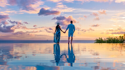 Young men and women watching the sunset with reflection in the infinity swimming pool at Saint Lucia Caribbean, couple at infinity pool during sunset in the evening light - obrazy, fototapety, plakaty