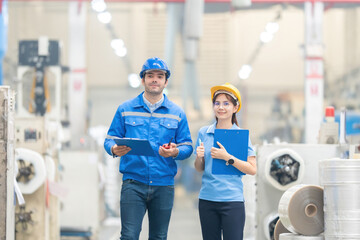 European male engineer and Asian female supervisor Walk around and inspect the machines working in the plastics and steel industry. Wear a uniform, safety helmet, and carry a note and radio.