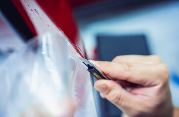 The process of installing protective film on the new red car.