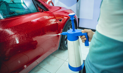 Worker in car service sprays water on the car before applying an protective film.