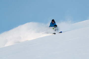 Skier is freeriding, downhill skiing, with powder rising up