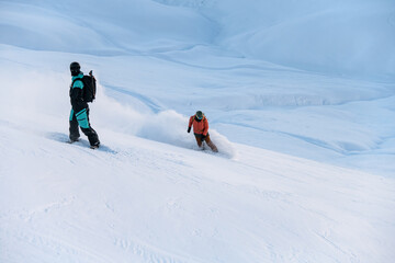Two snowboarders while standing on snowboards overcome ski track