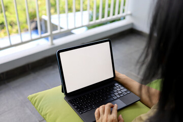 Amazing beautiful Asian woman working at home, sitting on rattan lounge chair while working with tablet computer on room balcony terrace.