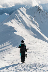 One-armed male snowboarder is walking on a snowy mountain along the ridge