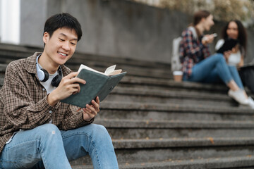 Obraz premium college student reading a book study on laptop prepare for the exam Or work on a group project while sitting on the steps of the university.