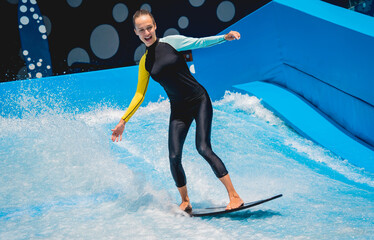 Beautiful young woman surfing on a wave simulator at a water amusement park