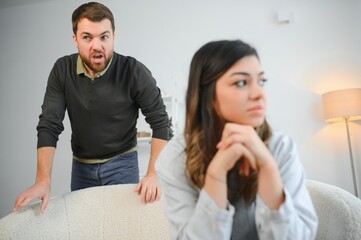 Emotional man gesturing and shouting at his wife, young couple having quarrel at home. Domestic abuse concept