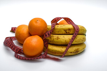 Owoce banany i pomarańcze leżą owinięte miara krawiecka na białym tle