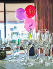 60th birthday balloons hanging from the window, selective focus on wine glasses on the table. Birthday celebration. Vertical format.