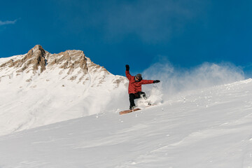 Snowboarder in a red jacket is going down a slope with his hands up for balance