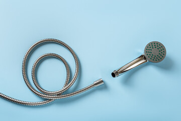 New hose and shower head over blue background. Coiled flexible hose and hand held shower head ready for changing. Washing, hygiene, bath and domestic plumbing work concept. © Maryia