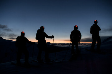Silhouettes of four skiers with flashlights on their foreheads on the mountain slope