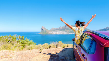 woman outside a car window with hands up, a car at Chapman's Peak Drive in Cape Town South Africa looking out over the ocean. women on a road trip at the garden route South Africa with a renal car - obrazy, fototapety, plakaty