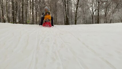 Mother with small child sledding in winter park. Family winter activities outdoors.