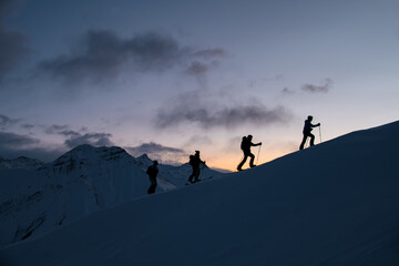 Silhouettes of four skiers on the highest point of the mountain against the background of the mountain peaks in the fog - obrazy, fototapety, plakaty