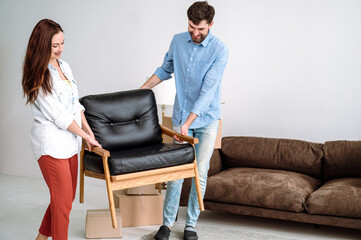 Happy smiling man and woman carry armchair in new home