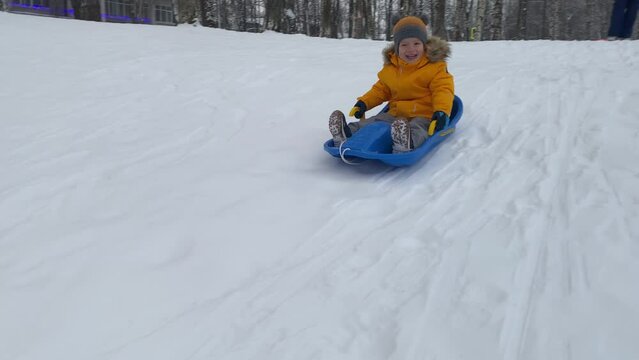Mother with small child sledding in winter park. Family winter activities outdoors.