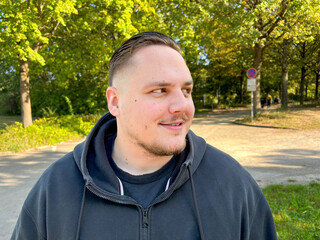 A young man with a hooded top and a black shirt standing in a park