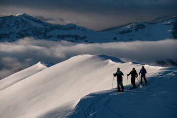 Three male skiers are standing on a snowy peak of a mountain