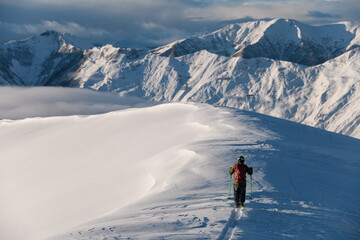 Fototapeta na wymiar Skier goes on a snowy mountain top on skis, helping himself with ski poles