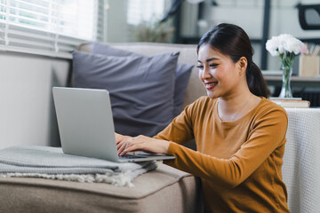 A beautiful Asian freelancer businesswoman is using a digital laptop near a window in her home office.