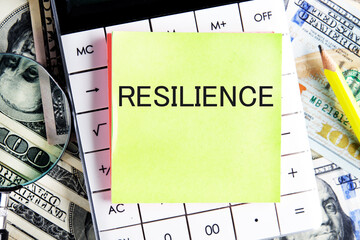 RESILIENCE text, a word written on a sticker lying on a calculator against a background of money