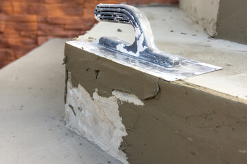 Close-up of trowel and fresh undried cement-based tile adhesive on stair.