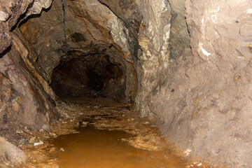 Old abandoned gold mine underground tunnel with rusty water lake. Dangerous tunnel full of dirt and rusty equipment.