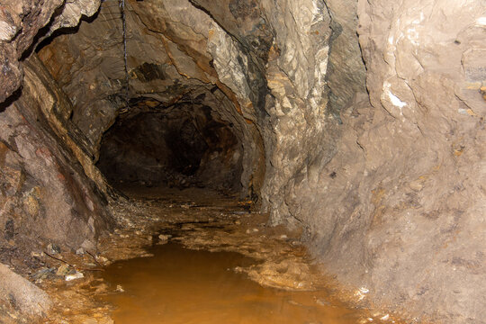 Old abandoned gold mine underground tunnel with rusty water lake. Dangerous tunnel full of dirt and rusty equipment.