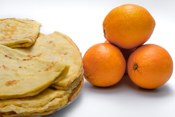 Pomarańcze leżą obko talerza z usmażonymi naleśnikami  - obrazy, fototapety, plakaty