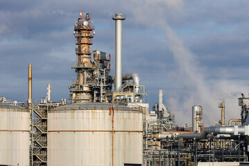 Refinery complex with fuel storage tanks, smokestacks and pipes with dark clouds