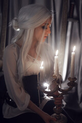 mystical photo by candlelight. a girl from a fairy tale with white hair in a medieval style sits on the floor in her room against the backdrop of burning candles