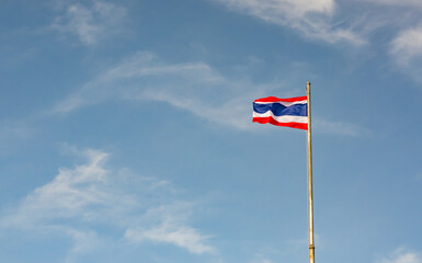 The flag of the Kingdom of Thailand shows horizontal stripes in the colors red  white  blue waving on white pole with blue sky and cloud background in clear day