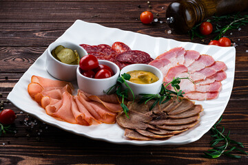 Meat plate with slices of sausage, ham, prosciutto, beef tongue, cherry tomatoes, pickles and sauce, banquet menu.