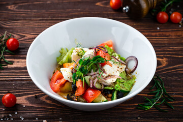 Greek salad of fresh cucumber, tomato, sweet pepper, lettuce, red onion, feta cheese, olives, oil and spices in a plate.