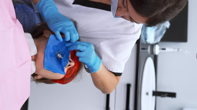 Dentist's hands in gloves with dental punch and cofferdam scarf. Dentist treats woman's tooth to patient with rubber dam. Modern dental office. Treatment elimination of caries, installation of filling