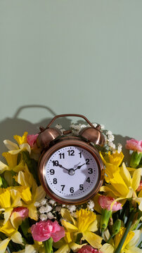Alarm clock with spring flowers on color background top view, flat lay. Daylight savings concept, spring forward