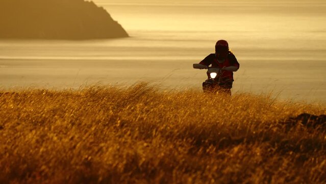 Silhouette of Extreme Pro Motocross Biker riding on back wheel opposite sunrise