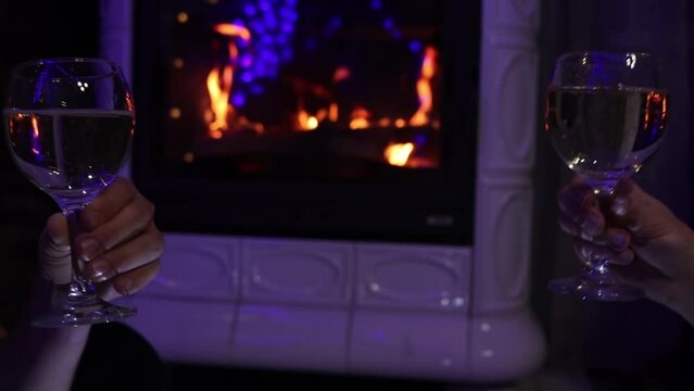 Young couple nearby fireplace sitting and clink wine glasses with champagne. New year or xmas celebration. Indoor shoot with unrecognizable people.
