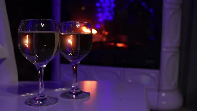 Closeup view of couple of champagne glasses nearby fire. Bubbles and fire reflections in wine glasses
