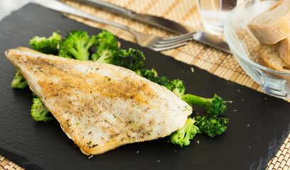 Fried fillet of sea bass with garnish of broccoli on black warm stone plate